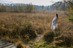 Zwangere vrouw poseert in lichtdoorlatende jurk met handen op buik in natuur